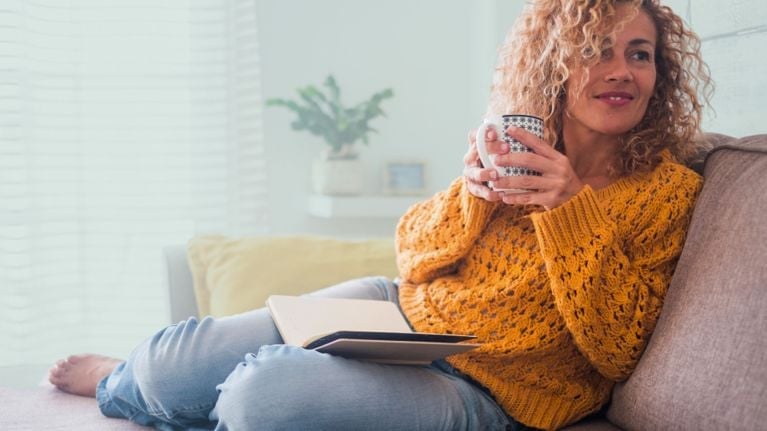 A woman with long dark hair is embracing a child. The child, facing away from the viewer, has their head resting on the woman's shoulder. The woman's eyes are closed, and she appears to be holding the child tenderly. The woman is wearing a light-colored top, and the child is wearing a yellow sweater. The background is a soft, blurred pink.