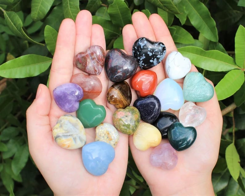 May include: A collection of heart shaped polished stones in various colors including red, green, blue, purple, white, yellow, brown, black, and gray.