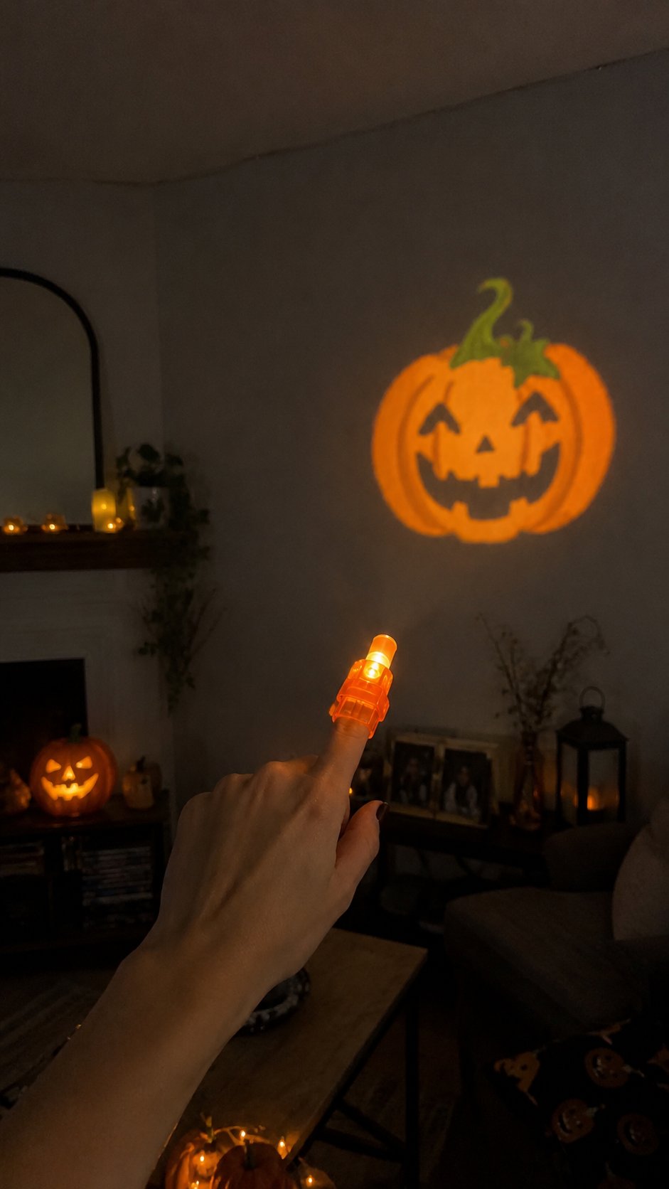 Vertical lifestyle photo of an orange finger projector casting a pumpkin pattern in a Halloween decorated living room